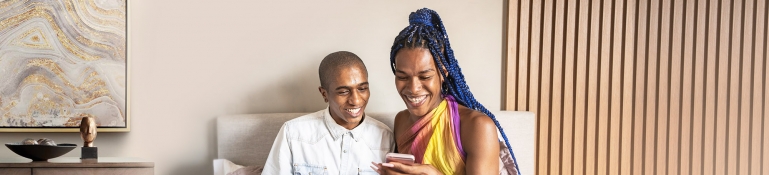 African American Non-binary person and transgender woman in bed using smart phone and talking.