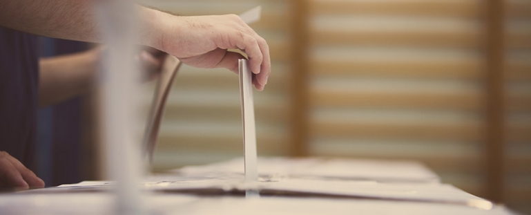 image of a persons hand placing a voting ballet in a box