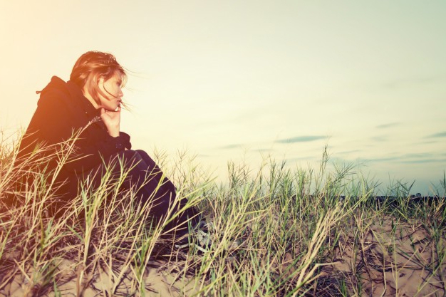 Photo of a worried girl sitting on the sand.