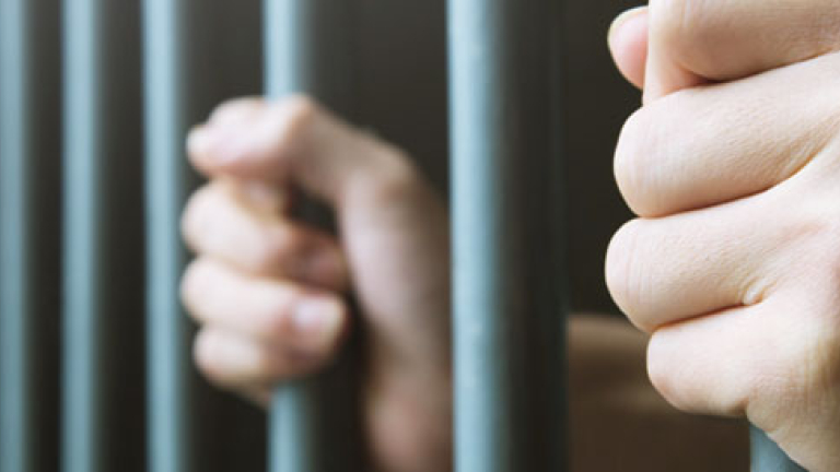 A person holding onto the bars of a jail cell.