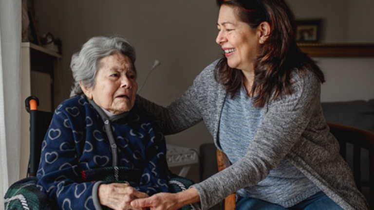 An older hispanic woman in a wheelchair being taken care at home by her adult daughter.