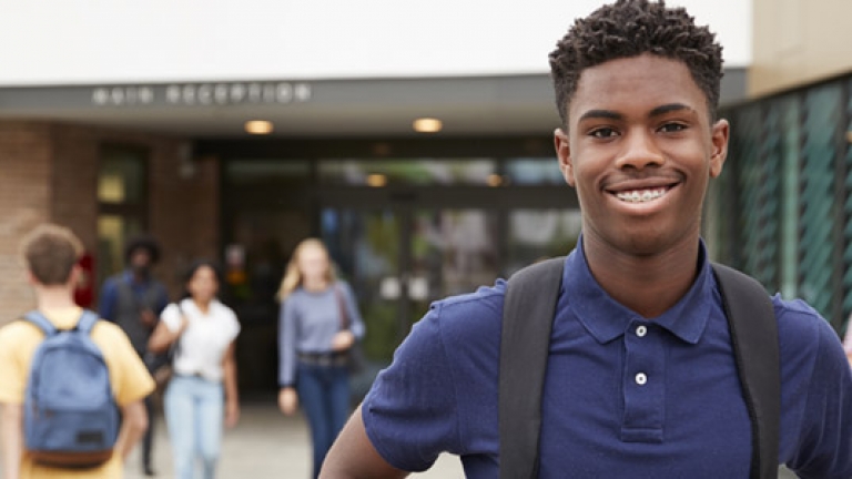 i young black student smiling in front of his school while other children enter.