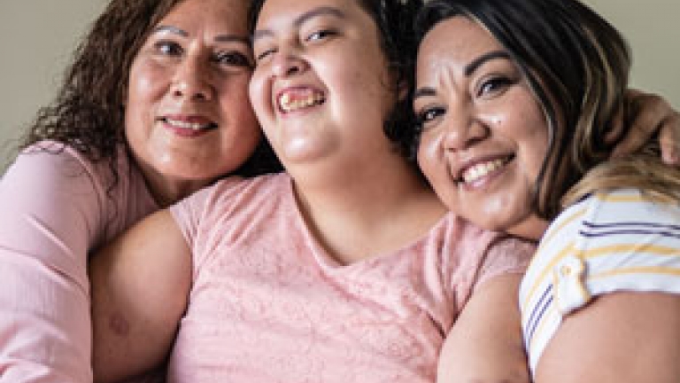 A Hispanic woman with a developmental disability smiling with her mother and her elder sister on either side of her.