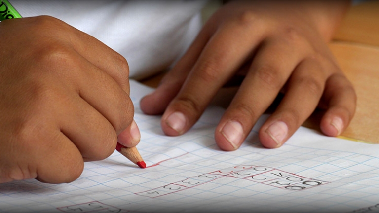 Photo of a close up of a little girls hands. She is solving a math problem on a piece of paper.