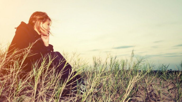 Photo of a worried girl sitting on the sand.